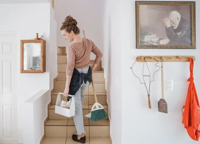 A cleaner carrying a caddy of cleaning supplies up a staircase in a rental property.