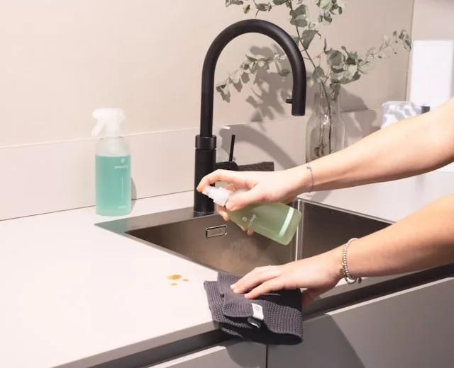 Hands cleaning a modern bathroom sink and tap.